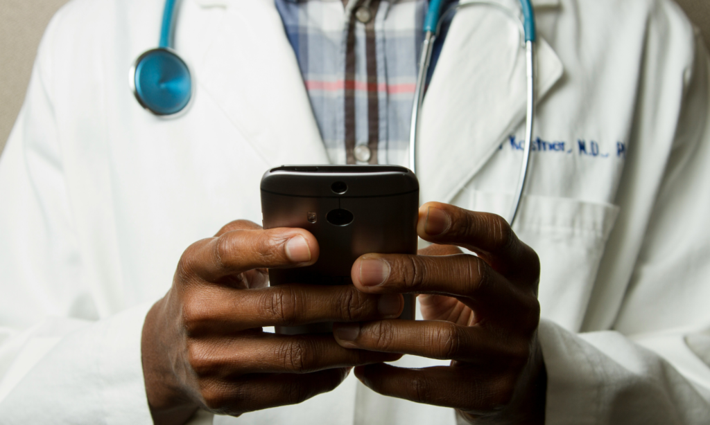 Doctor using a smartphone while wearing a white coat and stethoscope